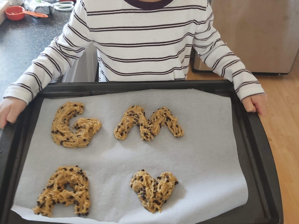 child holding baking tray with cookie dough shaped into letters on parchment paper