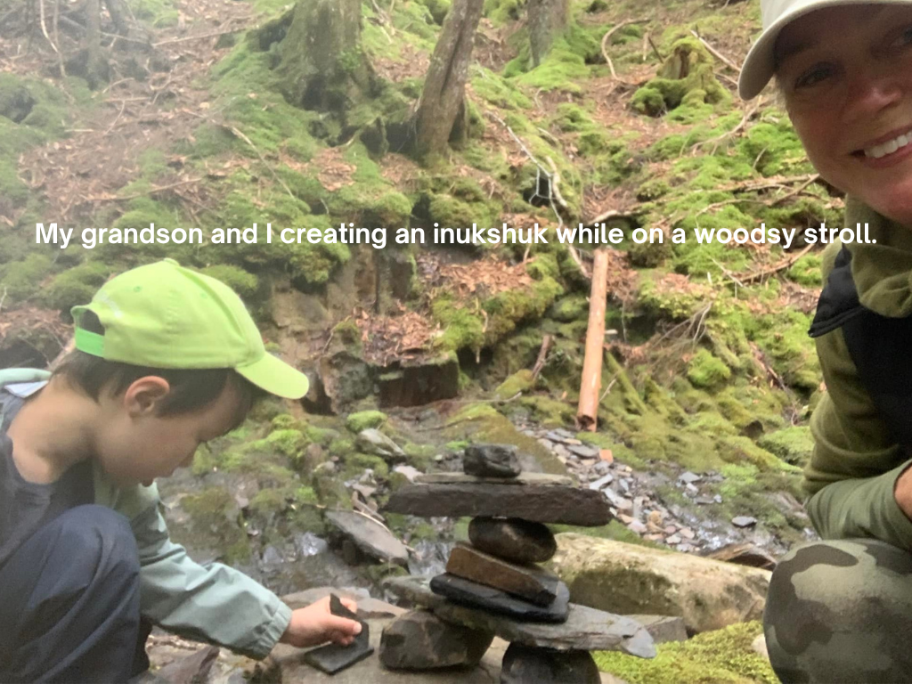 A child helps create an inukshuk by a forest brook. 